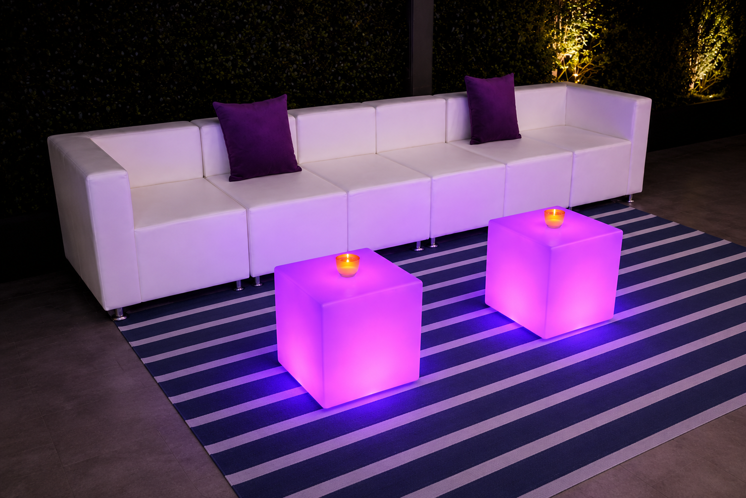 Long white modular sofa with candle-topped LED cubes outdoors
